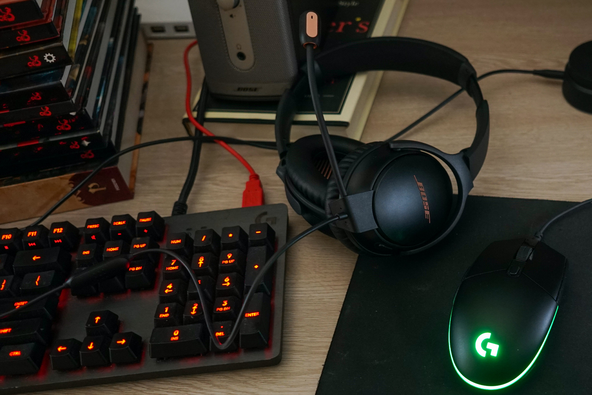 The Bose QuietComfort 35 II Gaming Headset sits on a desk next to Logitech gaming keyboard and gaming mouse, a Bose Companion speaker, and copies Dungeons and Dragons rulebooks, the Pathfinder Core Rulebook, and Dreyer's English