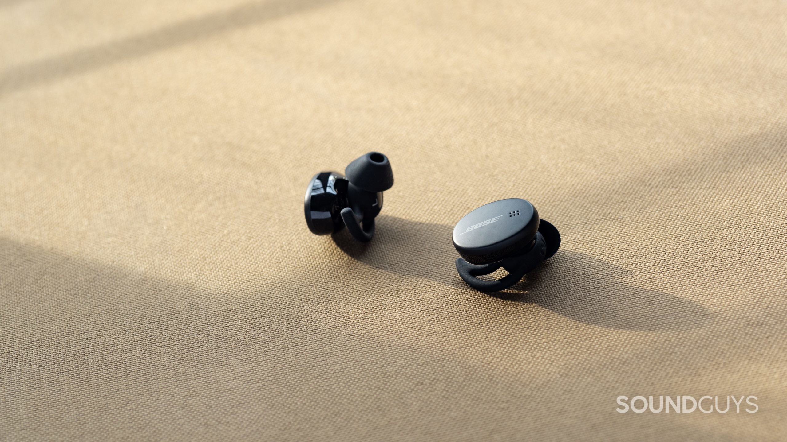 The Bose Sport Earbuds true wireless workout earbuds StayHear Max ear tips in view; the buds are against a beige background.