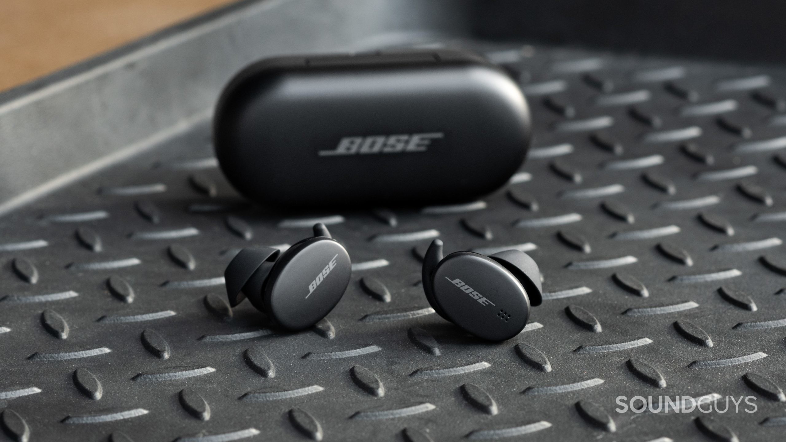 The Bose Sport Earbuds true wireless workout earbuds sit outside of the closed charging case, with the logos of the case and buds facing the viewer.