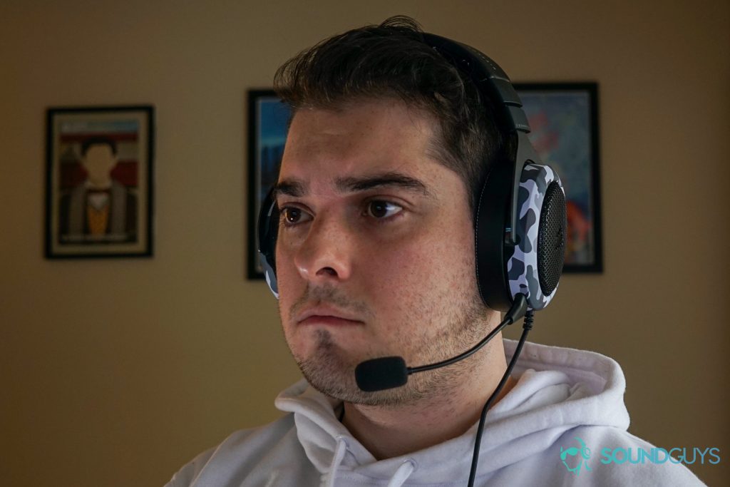 A man wears the Corsair HS60 Haptic gaming headset sitting at a desk with posters for My Brother, My Brother, and Me, and Canada Heritage Minutes in the background.