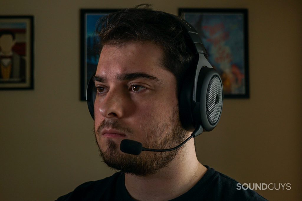 A man wears the Corsair HS75 XB Wireless gaming headset sitting at a PC, with a posters for My Brother, My Brother and Me, and Canadian Heritage Minutes