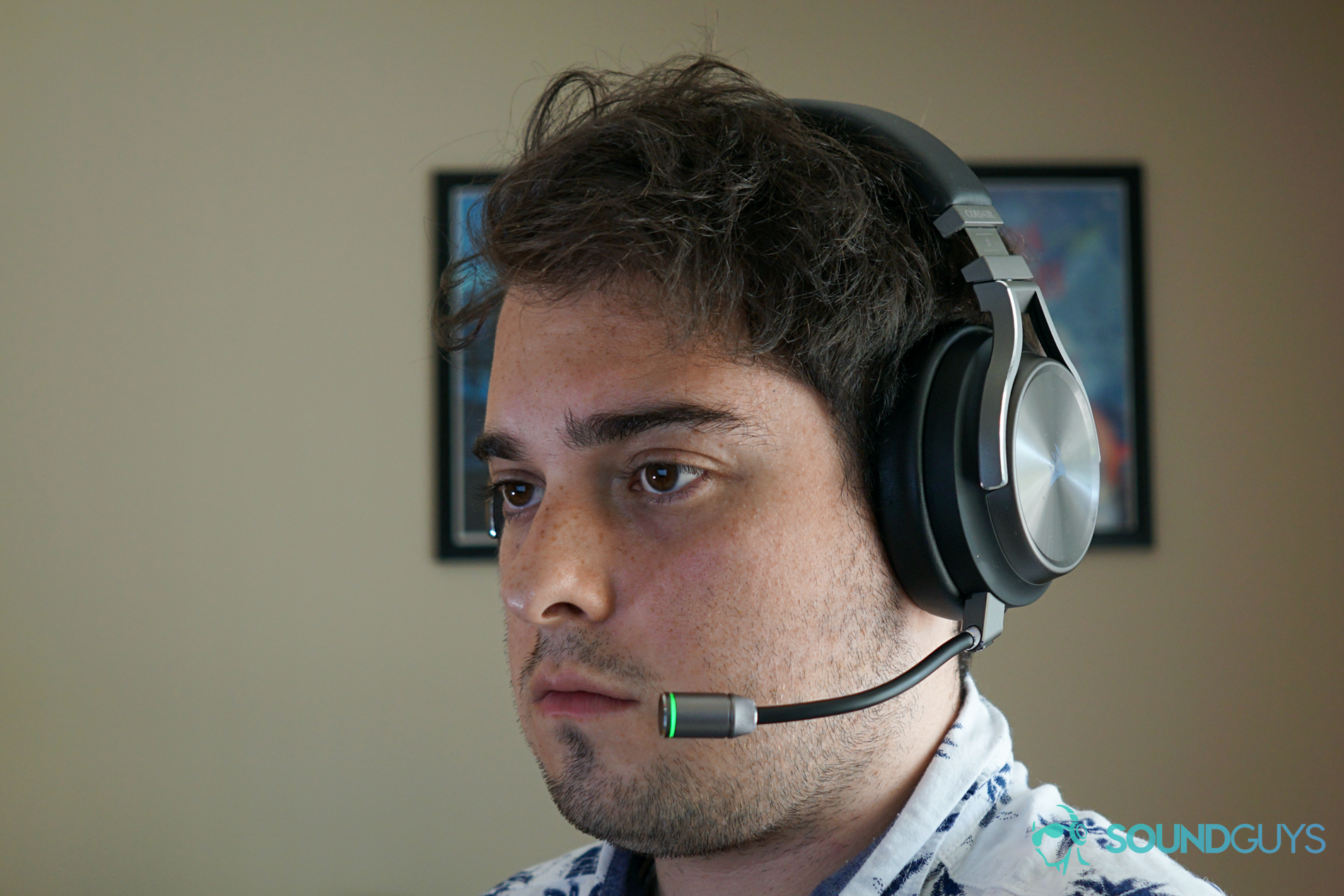 A man wears the Corsair Virtuoso Wireless SE sitting at a desk with posters for My Brother, My Brother, and Me in the background