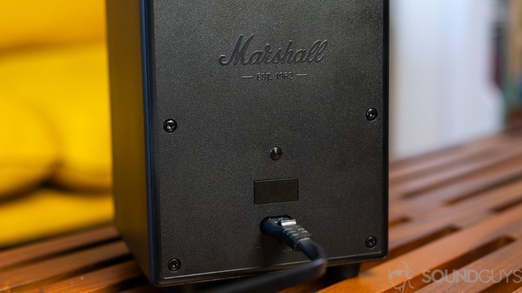 Close-up of Marshall Uxbridge Voice power supply and Bluetooth button on back fo the speaker which is on top of wooden coffee table