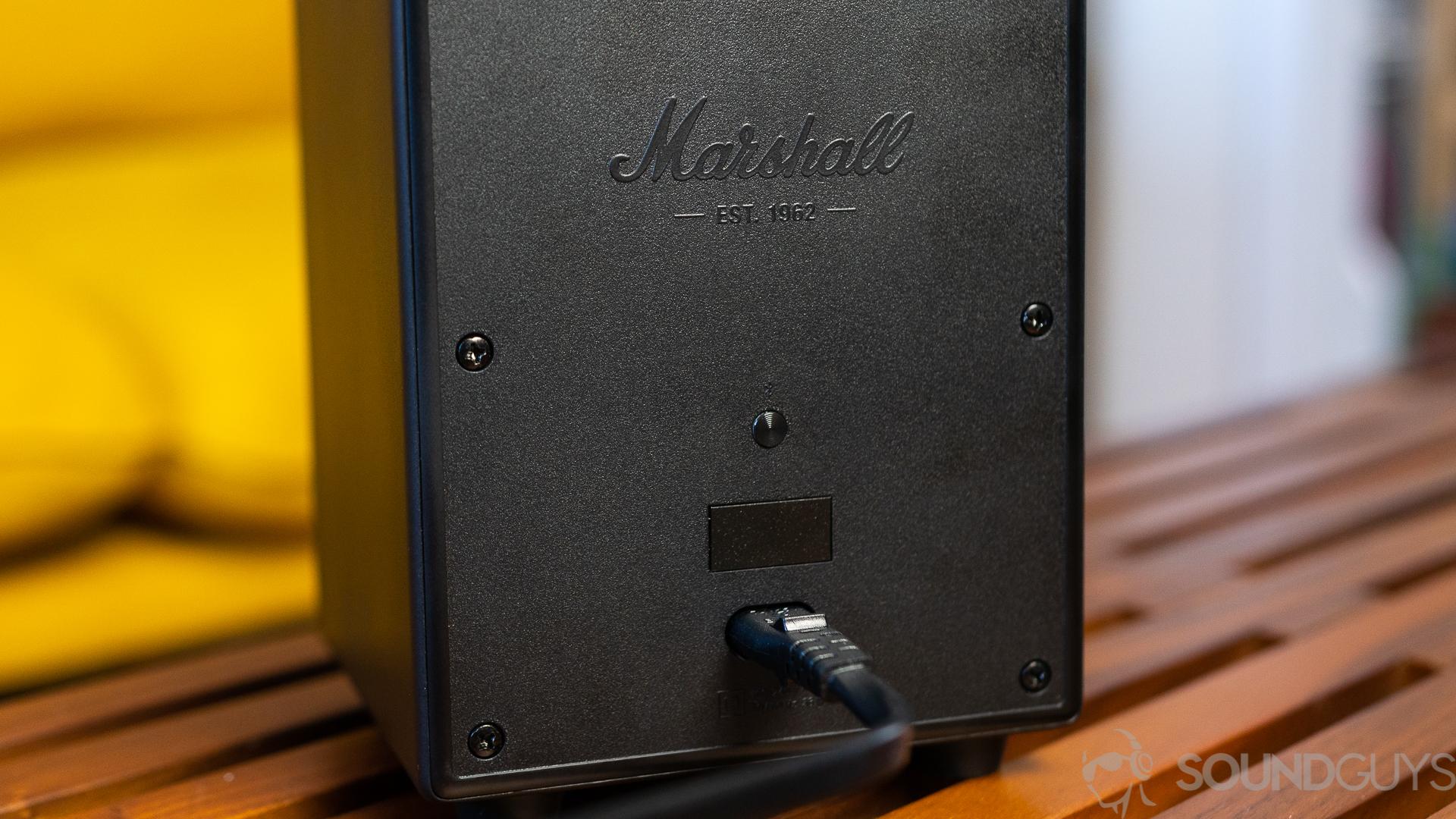 Close-up of Marshall Uxbridge Voice power supply and Bluetooth button on back fo the speaker which is on top of wooden coffee table