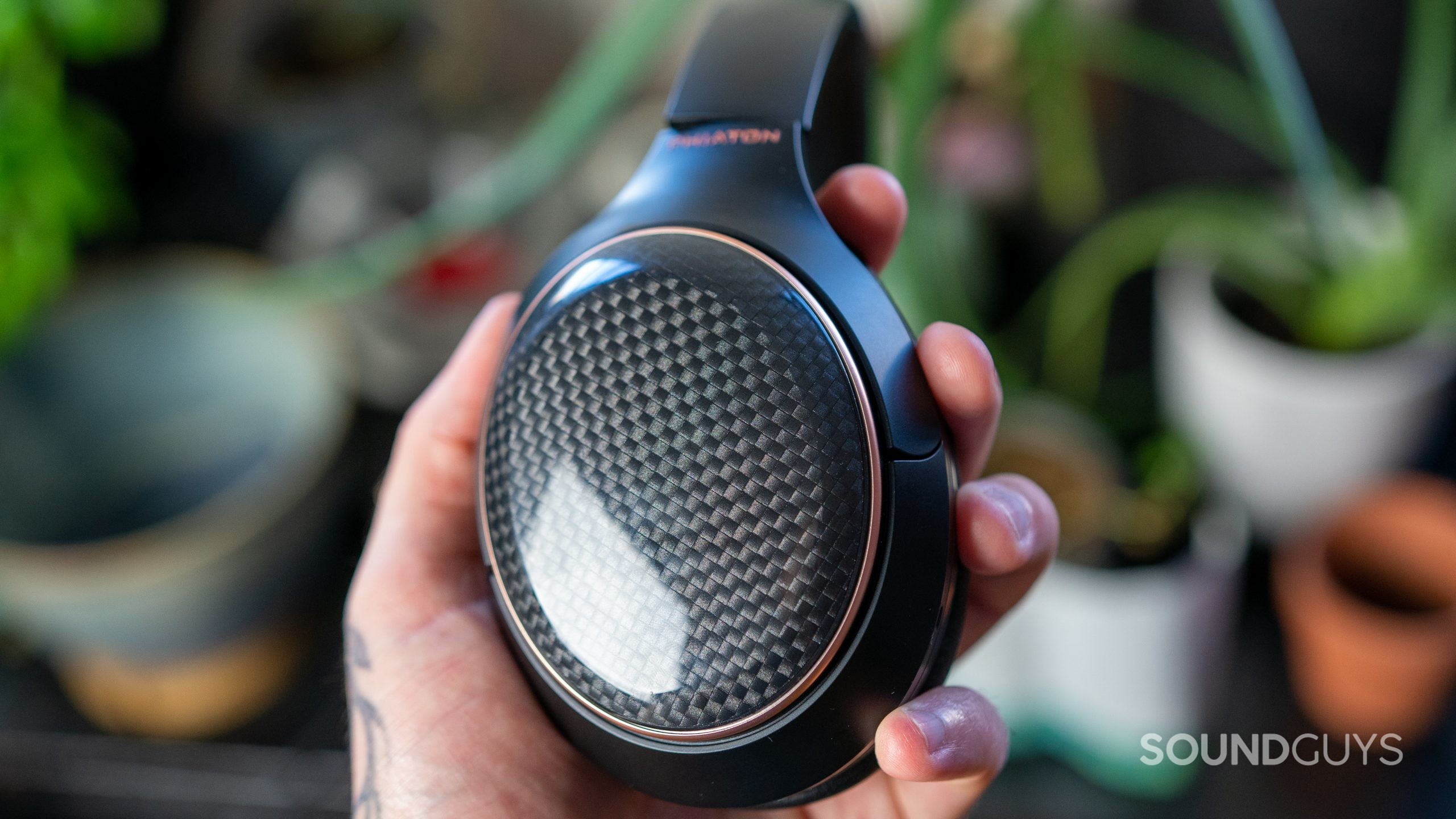 A man holds the Phiaton 900 Legacy headphones in hand in front of plants.
