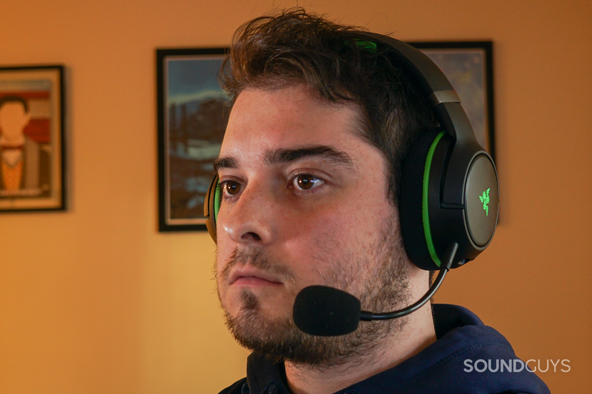 A man wears the Razer Kaira Pro gaming headset seated a PC with posters for My Brother, My Brother, and Me.