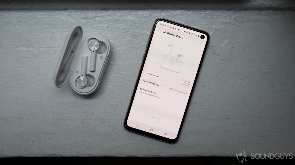 The OnePlus Buds Z cheap true wireless earbuds sit in the charging case next to a smartphone with the HeyMelody headphones app open.