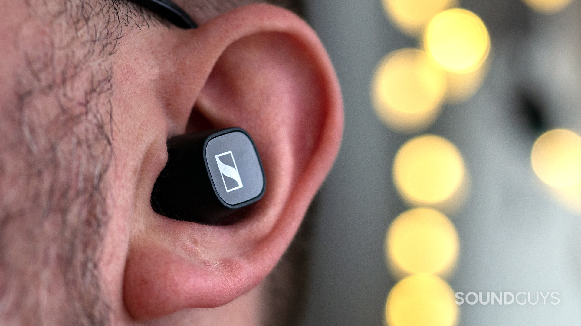 sennheiser-cx-400bt-earbuds-ear A photo showing the Sennheiser CX 400BT in a man's ear, with fairy lights in the background.
