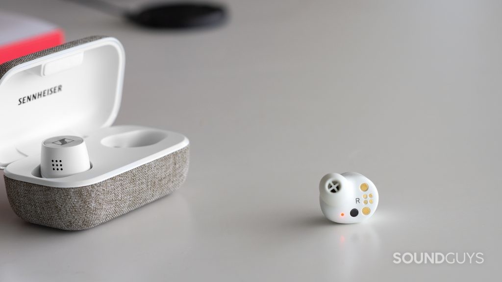 One of the Sennheiser MOMENTUM True Wireless 2 earbuds rests outside of the open charging case, while the other remains inside.
