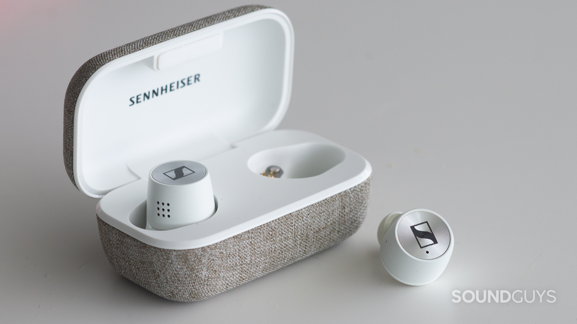 A photo of the Sennheiser Momentum True Wireless 2.0, with the left earbud in the case, and the right earbud sitting on a table.