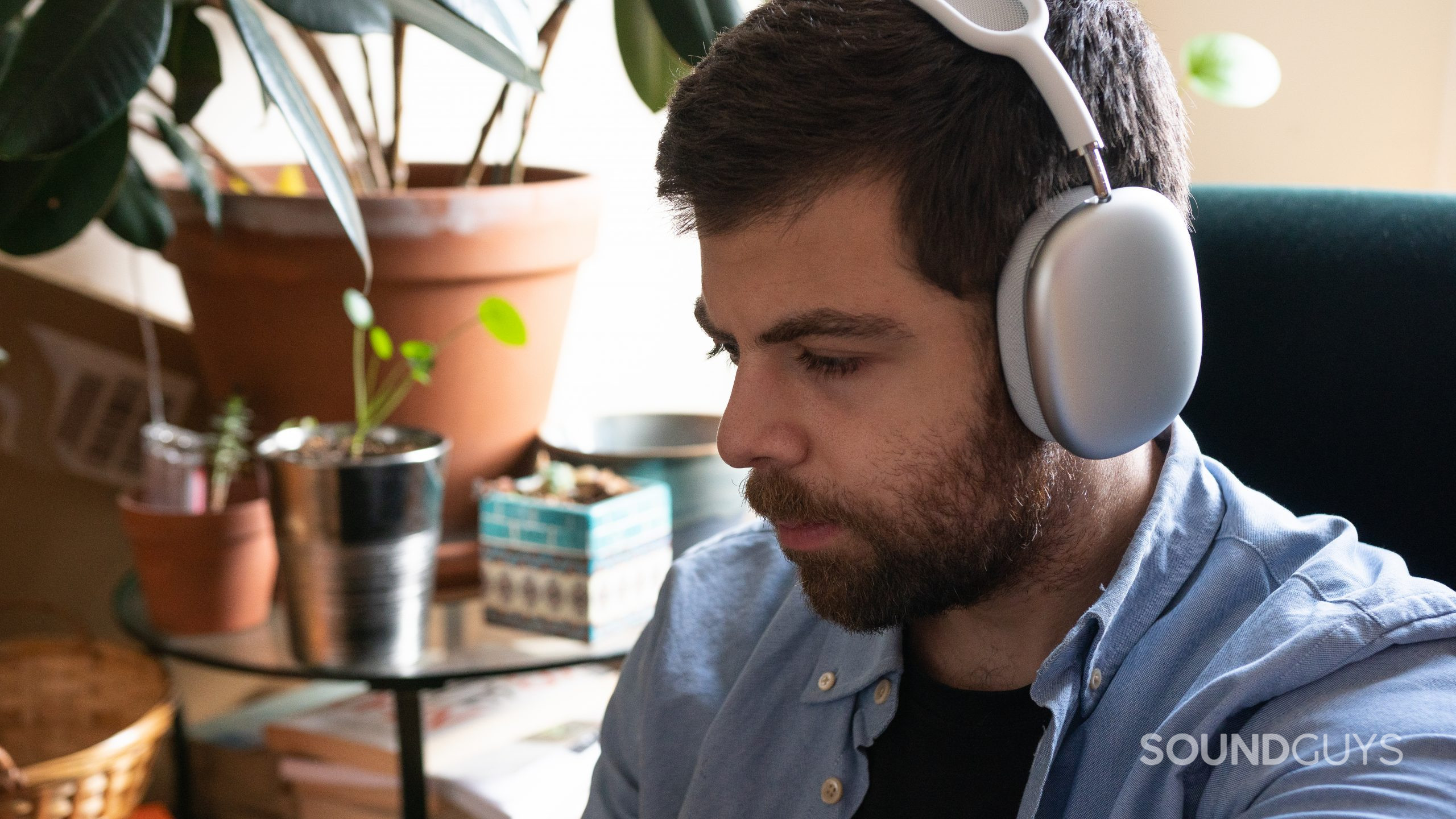 A man wears the white Apple AirPods Max while sitting in green chair.