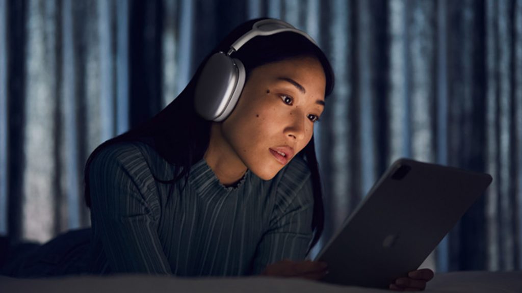 A woman listens to the Apple AirPods Max noise cancelling headphones in white while she uses an iPad.