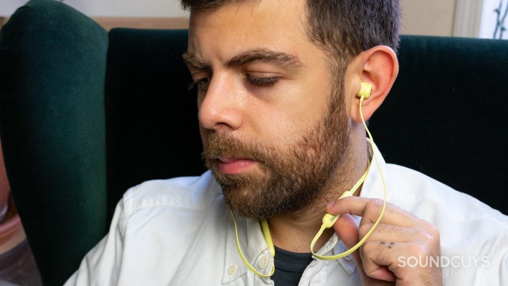 A man presses the button on Beats Flex earbuds.