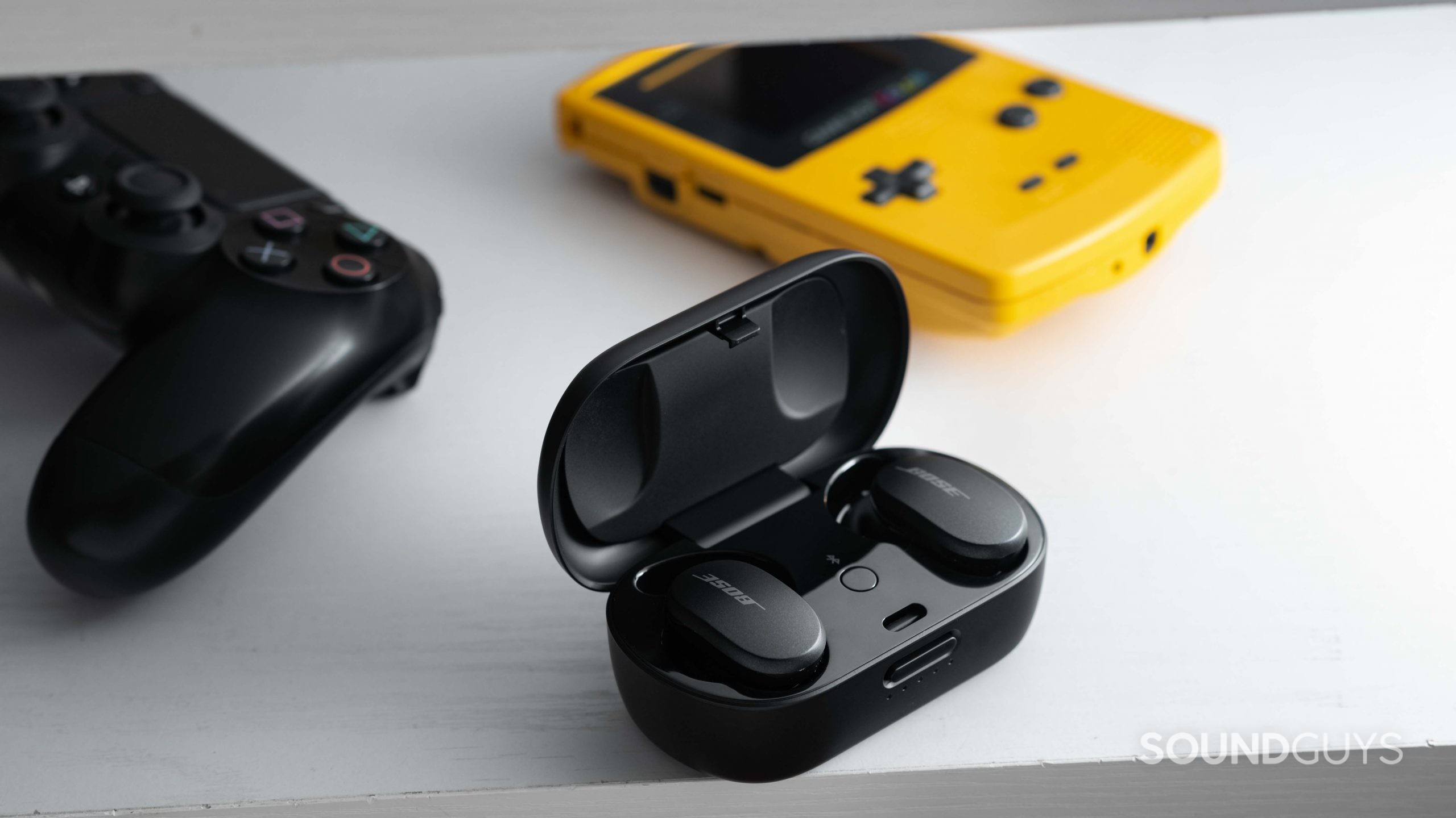 The Bose QuietComfort Earbuds noise canceling true wireless earbuds in the USB-C charging case next to a Gameboy Color and PlayStation 4 controller.