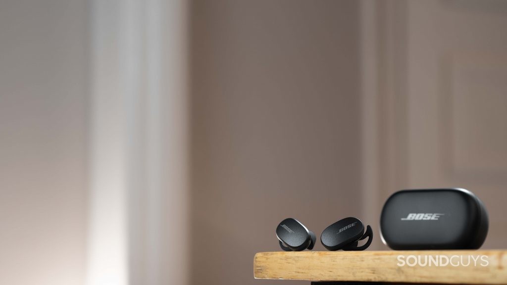 The Bose QuietComfort Earbuds noise cancelling true wireless earbuds rest next to the closed charging case on a wood surface.