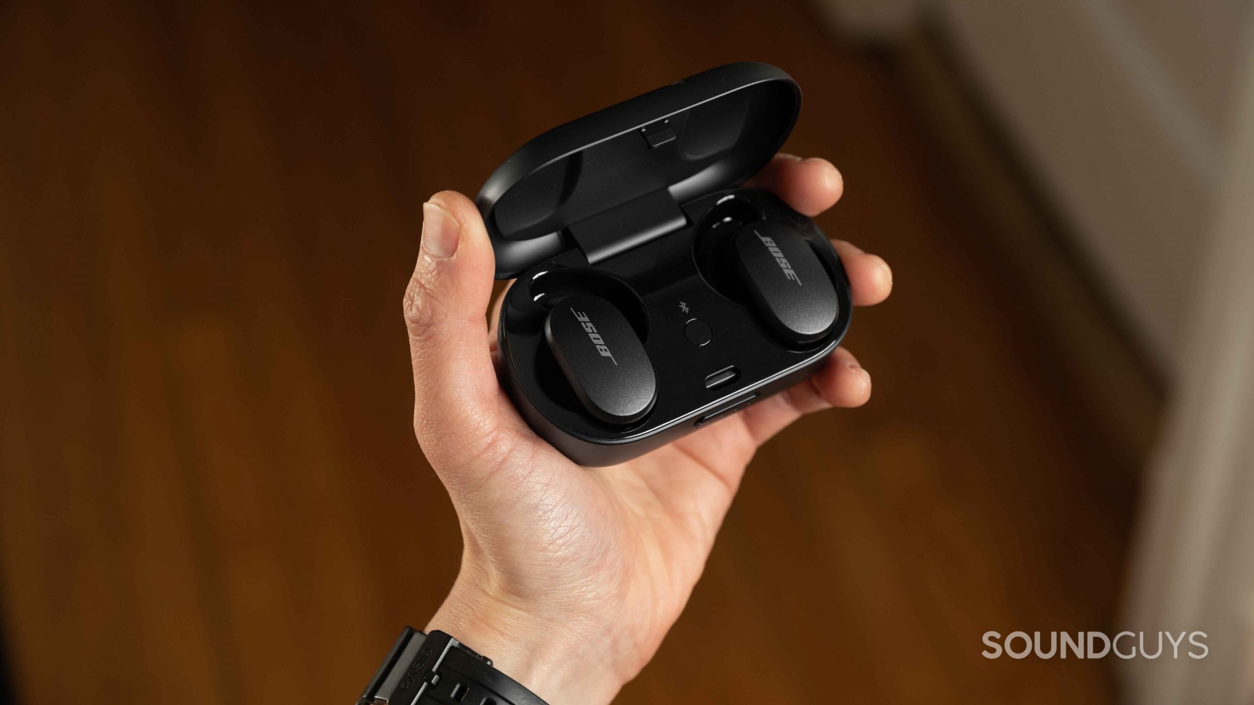 A hand holds the Bose QuietComfort Earbuds noise canceling true wireless earbuds open charging case.