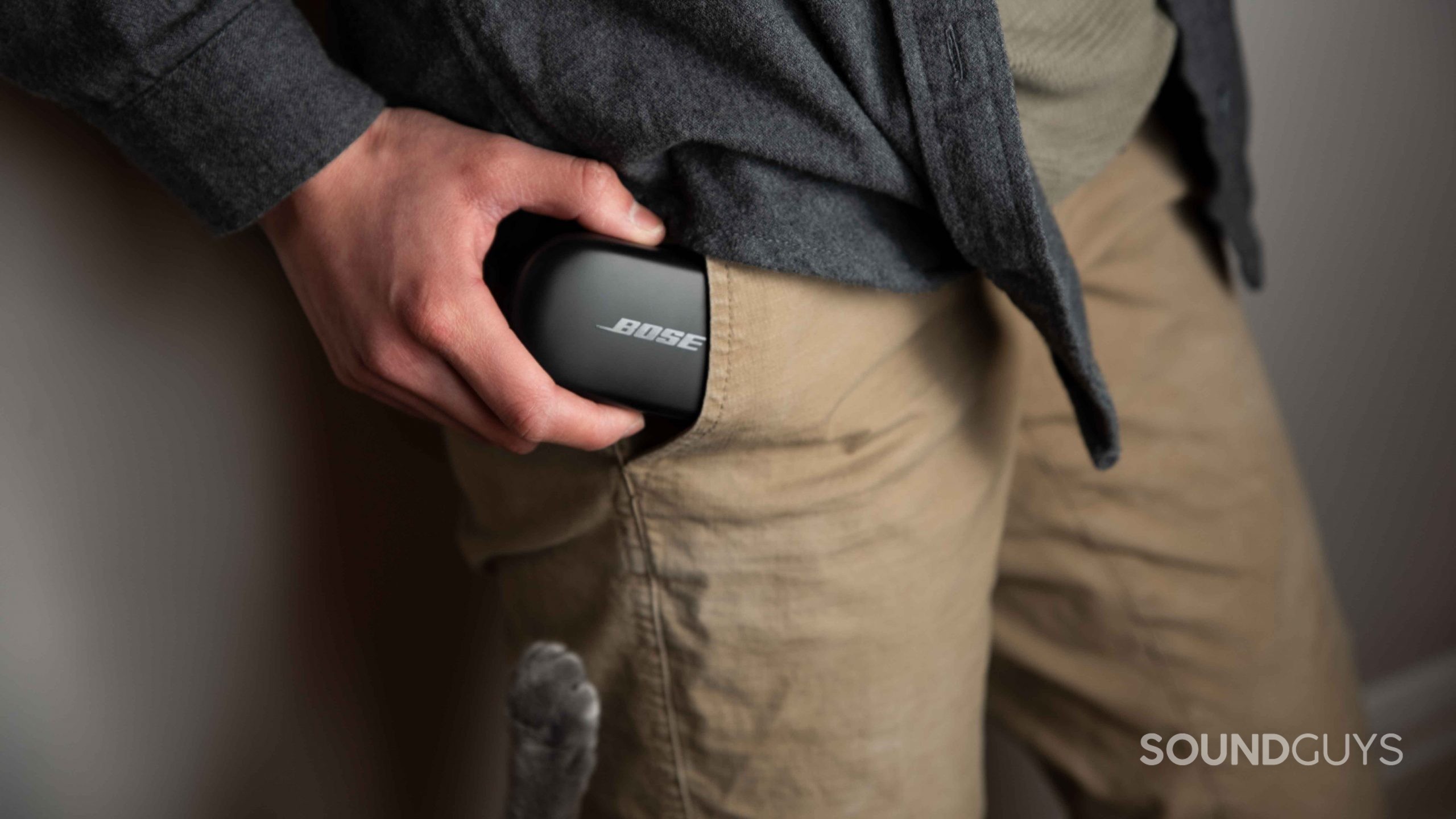 A cat paw reaches for the Bose QuietComfort Earbuds case as a woman inserts it into her pants pocket.