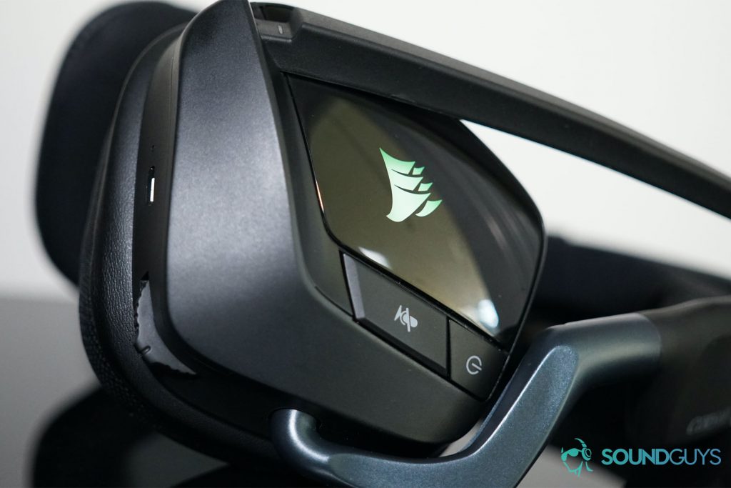 The Corsair Void RGB Elite Wireless gaming headset lies on its side, with its in ear controls visible and its RGB lights on.