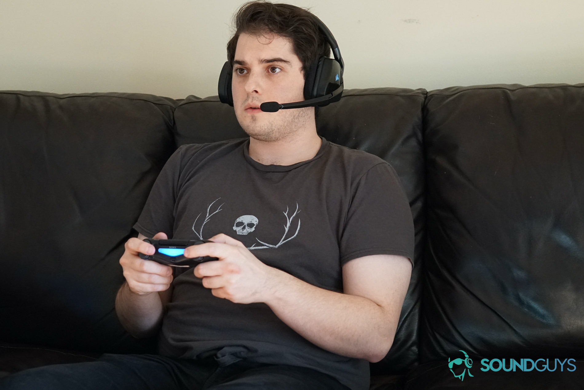A man seated on a couch using the Corsair Void RGB Elite Wireless gaming headset while playing Dauntless on Playstation 4.