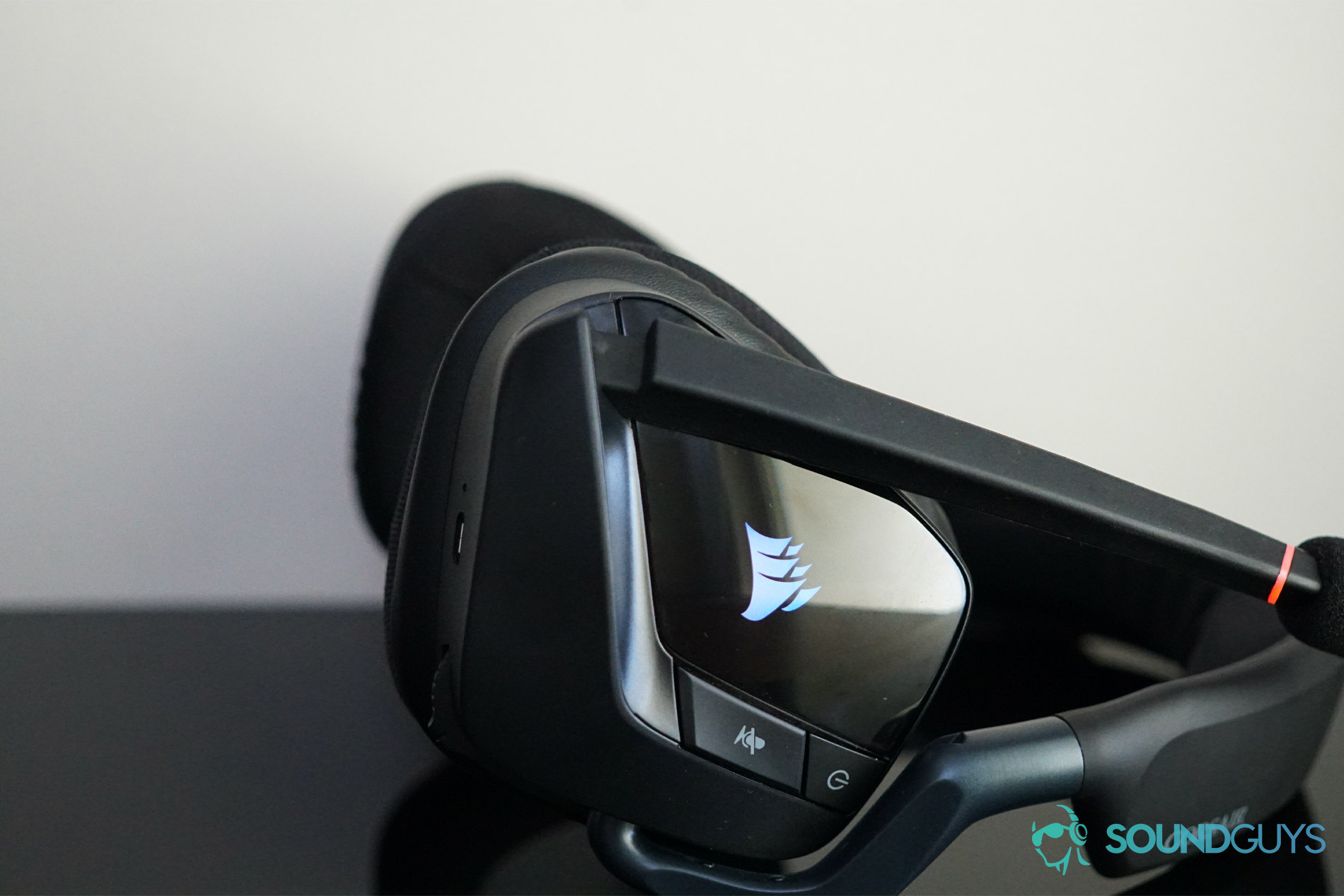 The Corsair Void RGB Elite Wireless gaming headset lies on its side, with its in ear controls visible and its RGB lights on.