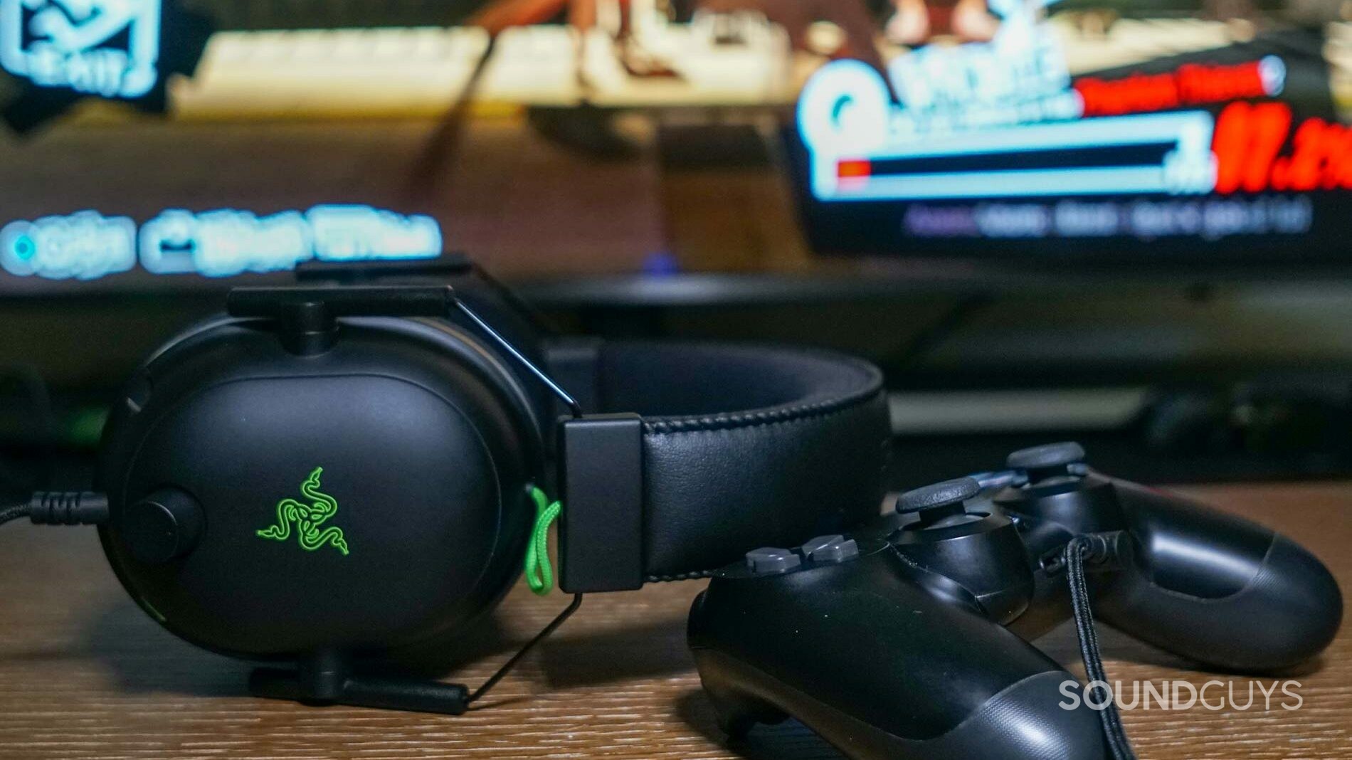 The Razer BlackShark V2 gaming headset sits on a wooden table, leaning on a PlayStation DualShock 4 controller in front of a television with Persona 5 Royal on it.