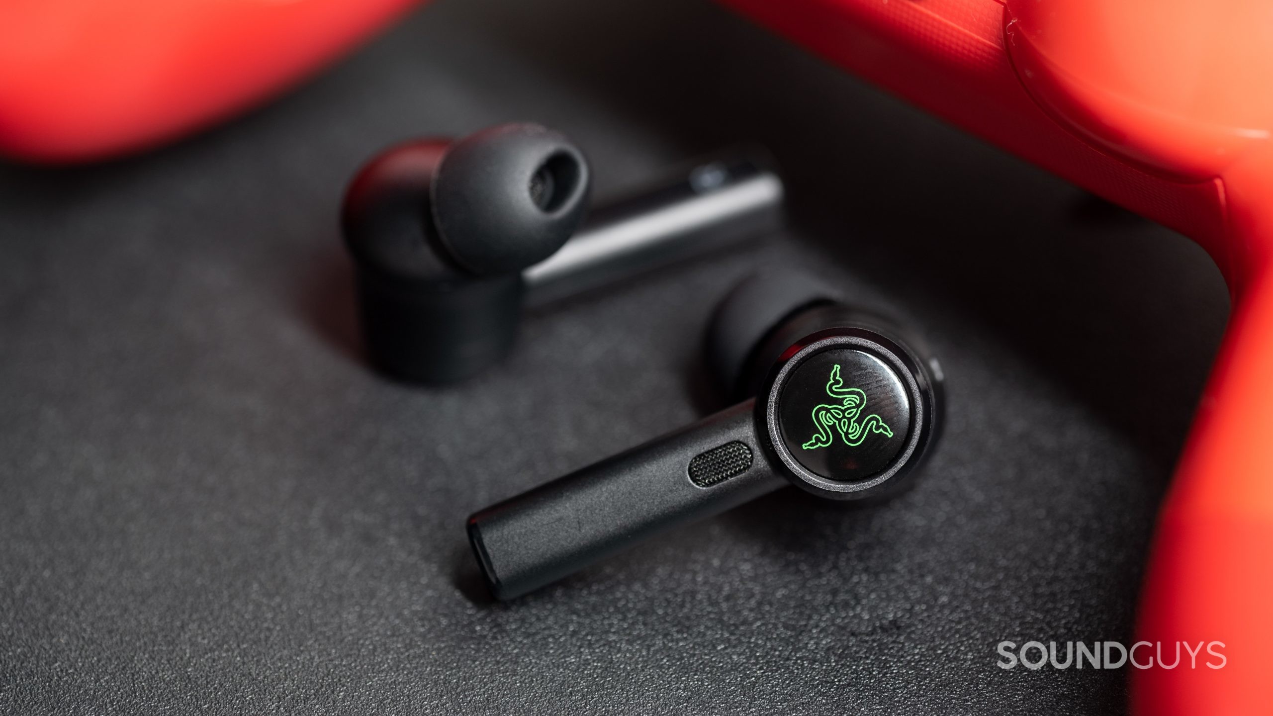The Razer Hammerhead True Wireless Pro noise canceling earbuds oblong ear tips attached to the buds beneath a PlayStation 4 controller in red.