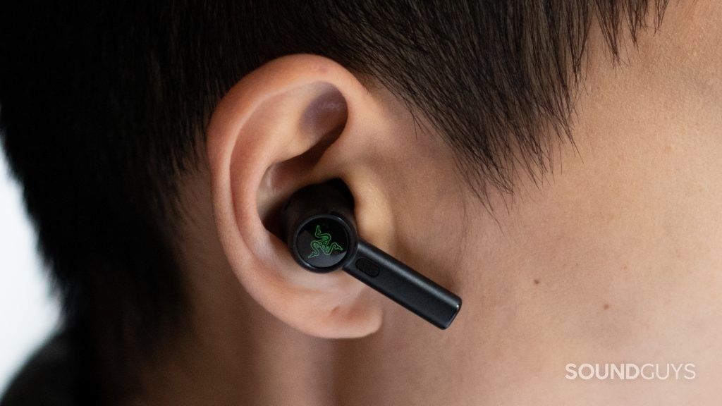 A hand holds the Razer Hammerhead True Wireless Pro noise canceling earbuds sit in a woman's ear.