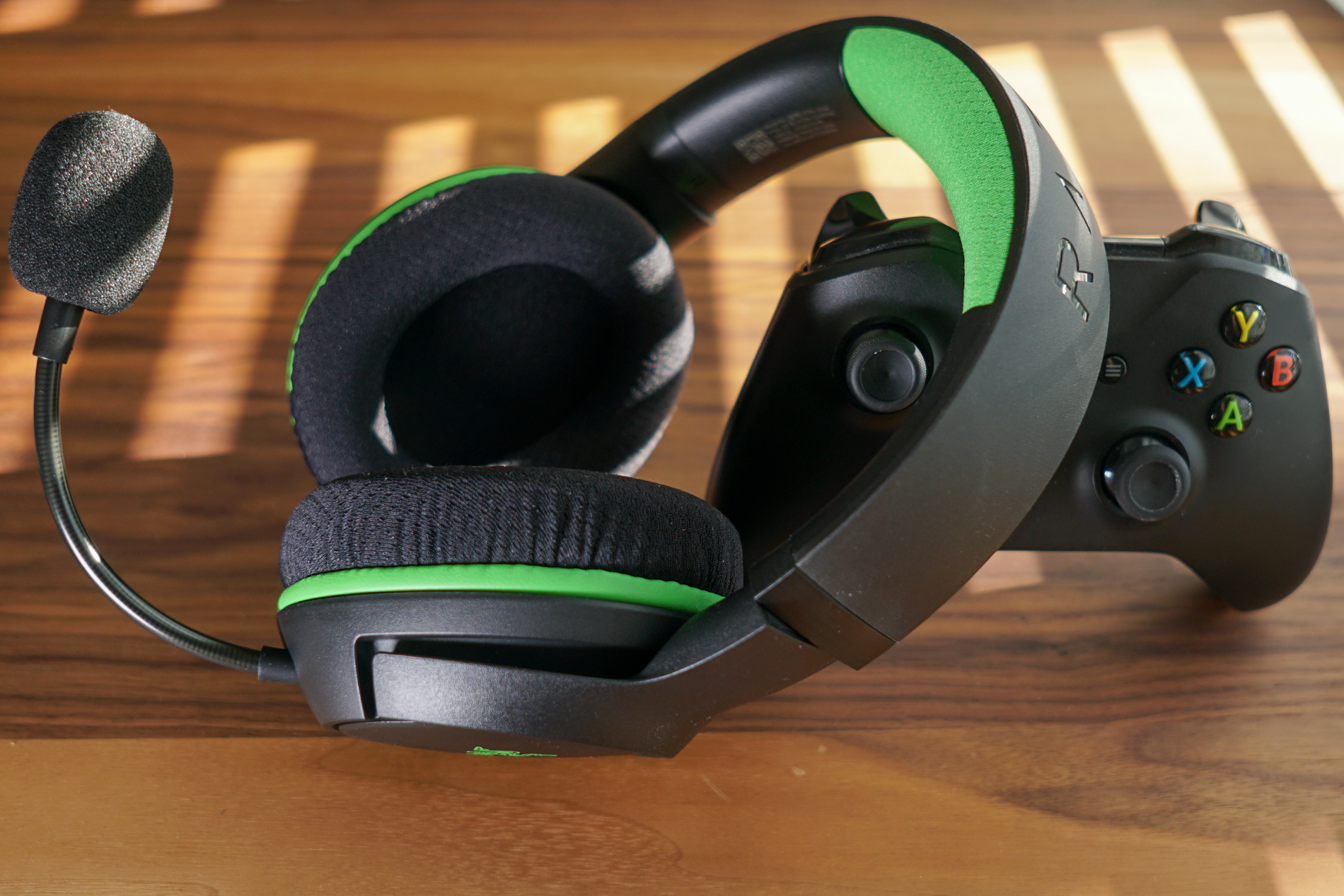 The Razer Kaira Wireless leans on an Xbox One controller on a wooden table near a window with the blinds drawn