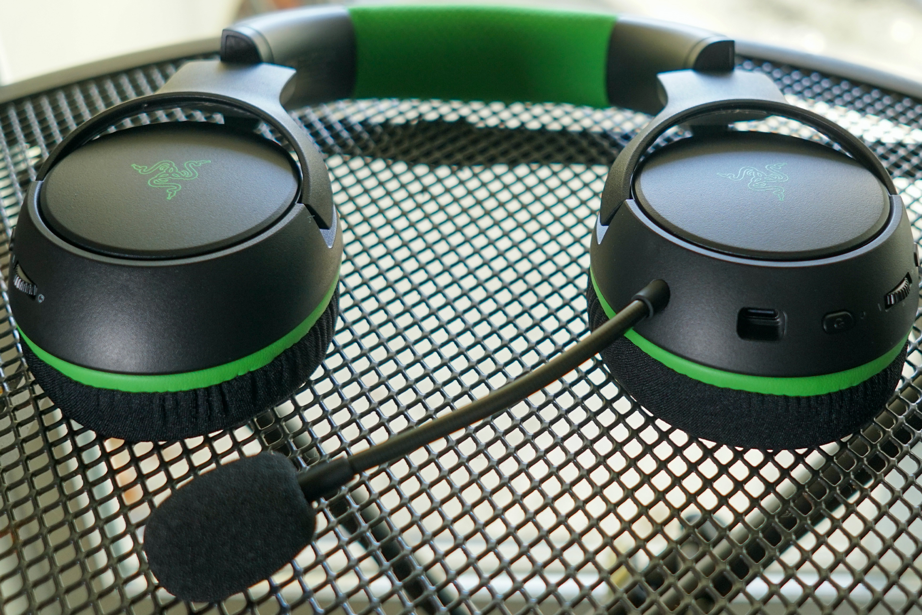 The Razer Kaira Wireless lays flat on a wireframe table displaying its controls and charging port.