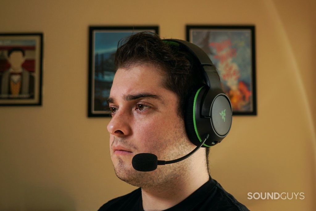 A man wears the Razer Kaira Wireless sitting at a computer, with posters for My Brother, My Brother and Me, and Canada Heritage Minutes in the background.