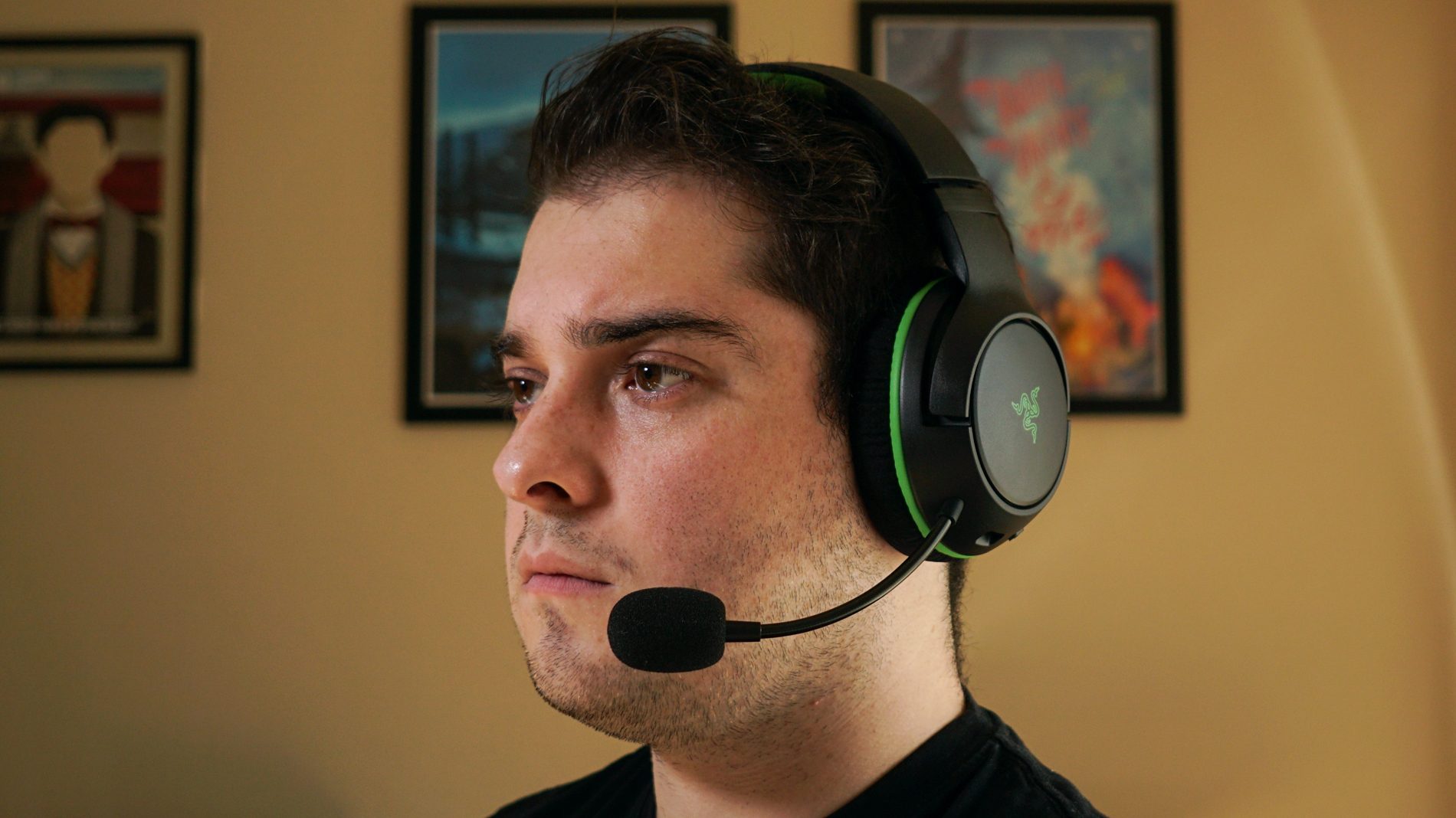 A man wears the Razer Kaira Wireless sitting at a computer, with posters for My Brother, My Brother and Me, and Canada Heritage Minutes in the background.