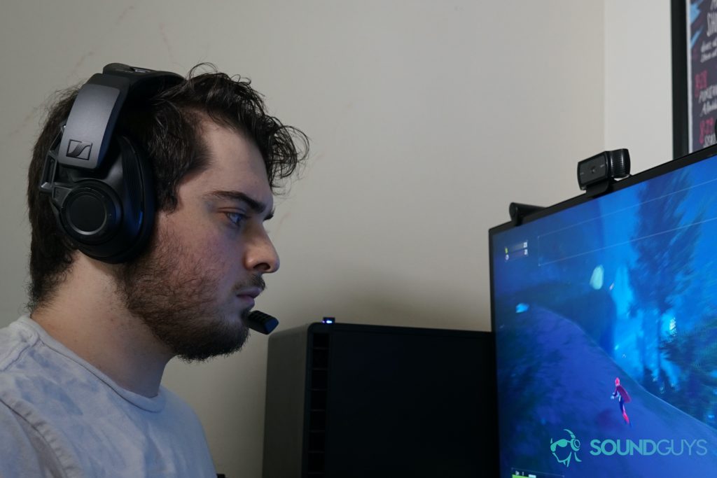 A man sits a computer running Risk of Rain 2 while wearing the Sennheiser GSP 670.