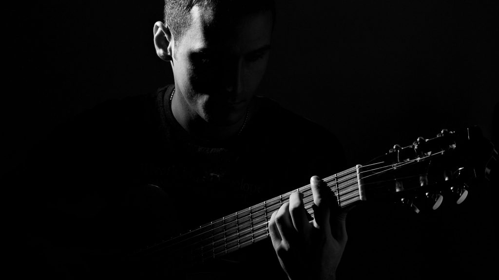 A man plays guitar; this is a darkly lit grayscale image.