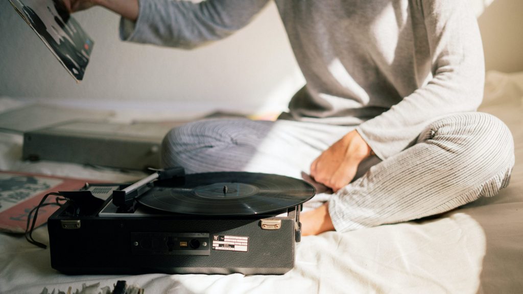 A person sits on a bed with vinyl records and a record-player.