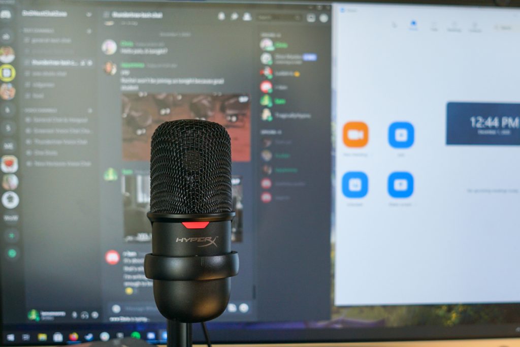 The HyperX solocast sits on a stack of books in front of a monitor with Discord and Zoom open.