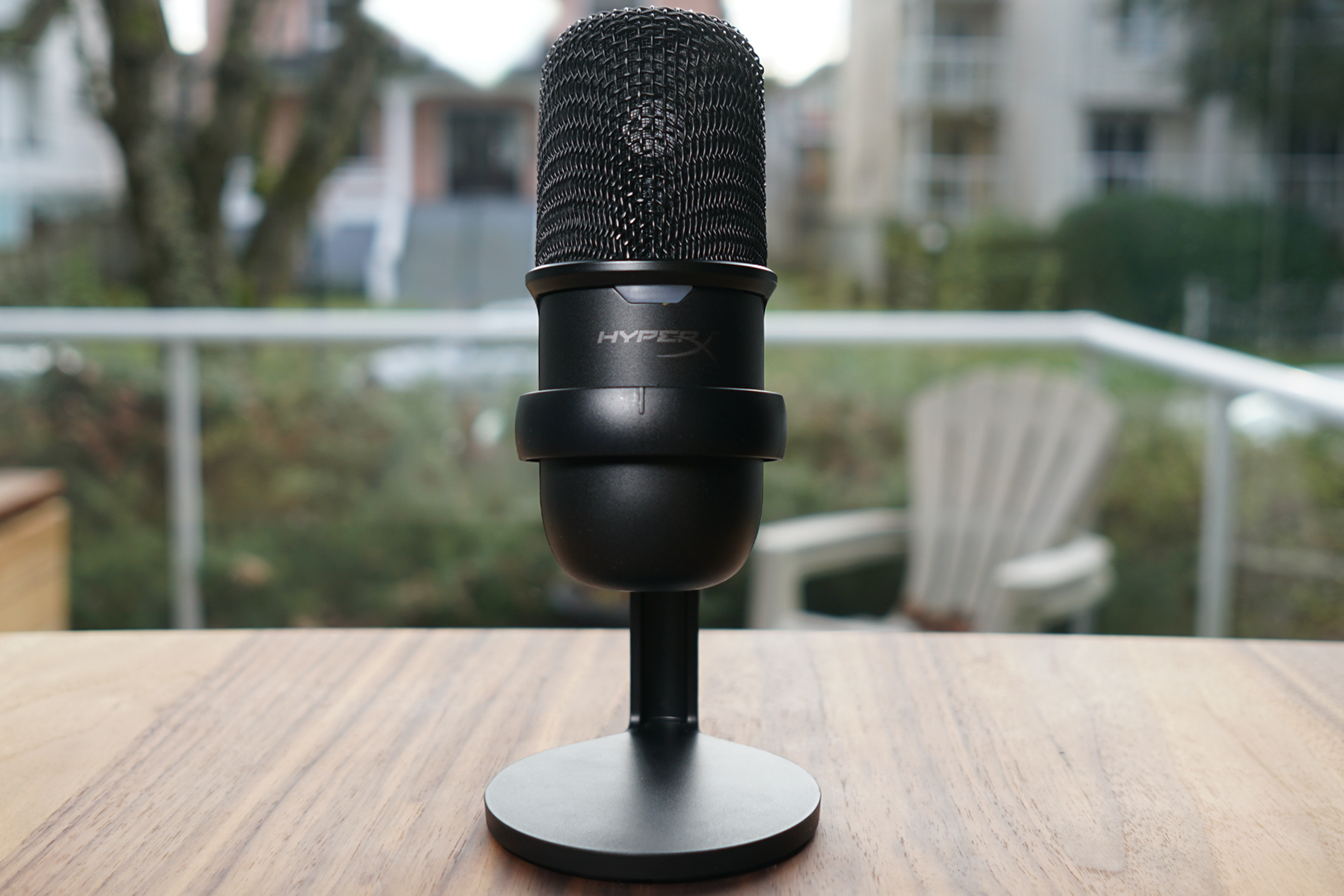 The HyperX Solocast stands on a wooden table in front of a window.