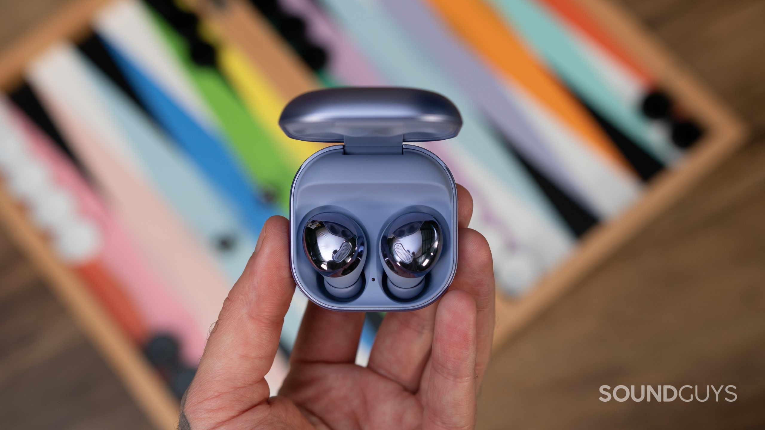 A man holds open case of Samsung Galaxy Buds Pro in hand over colorful game.