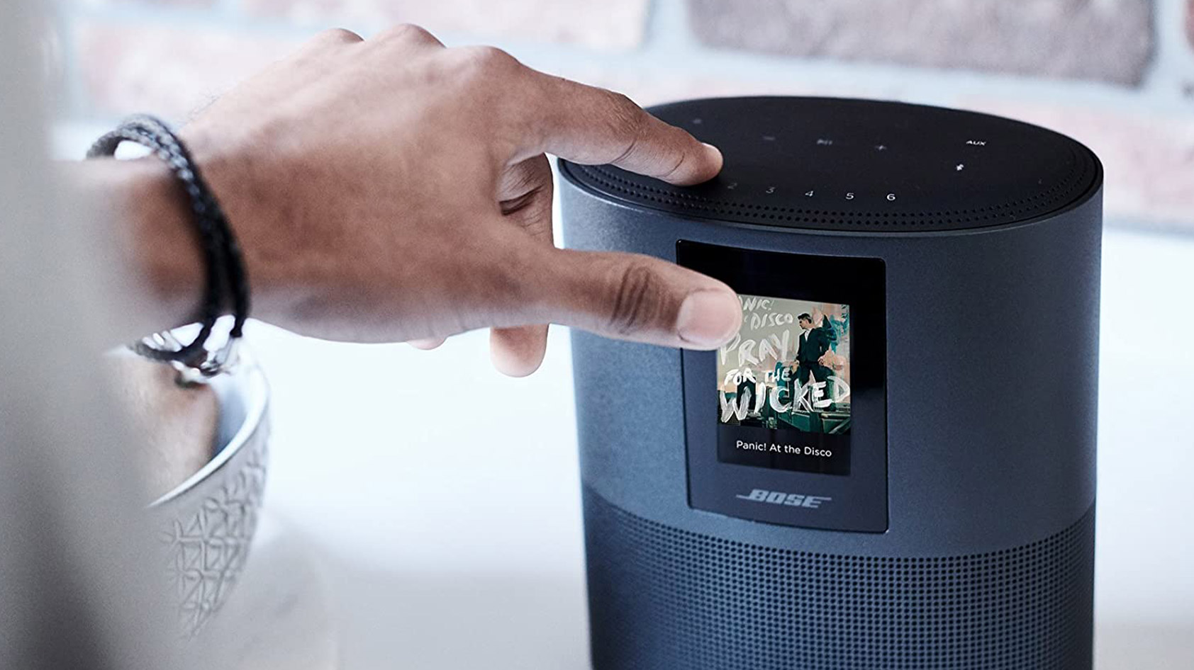 A man touches the panel on the top of the Bose Home Speaker 500 to adjust playback.