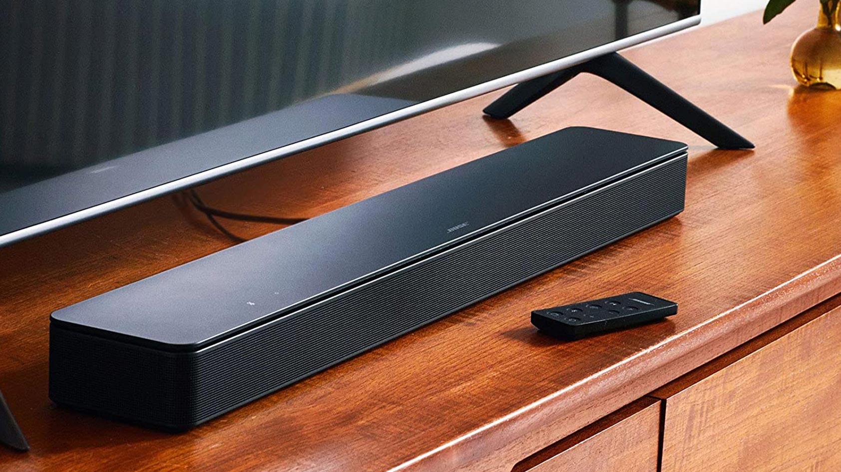 The Bose Smart Soundbar 300 on a wood TV stand with the remote in front of it.