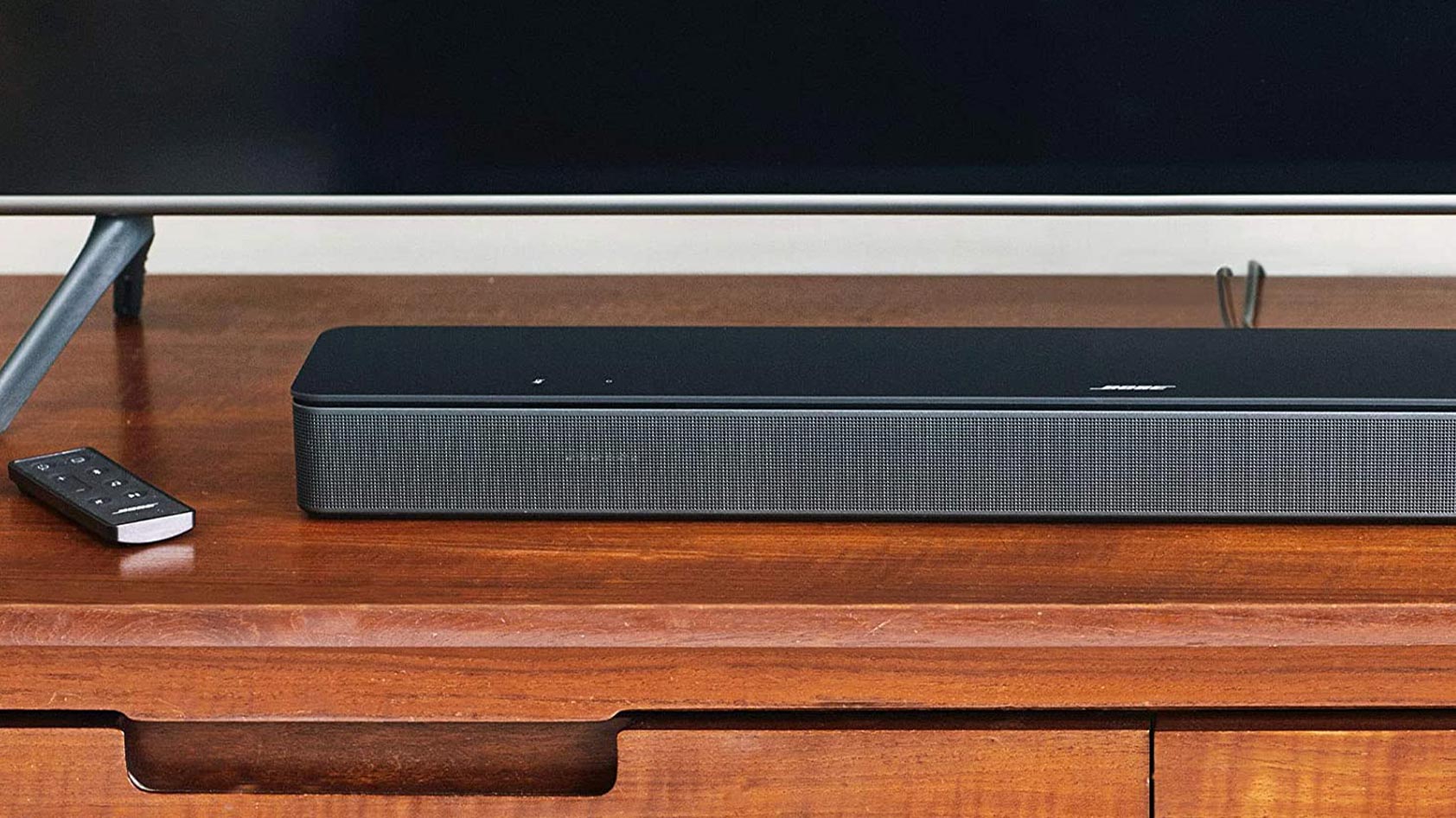 The Bose Smart Soundbar 300 lies on a TV stand next to the remote.