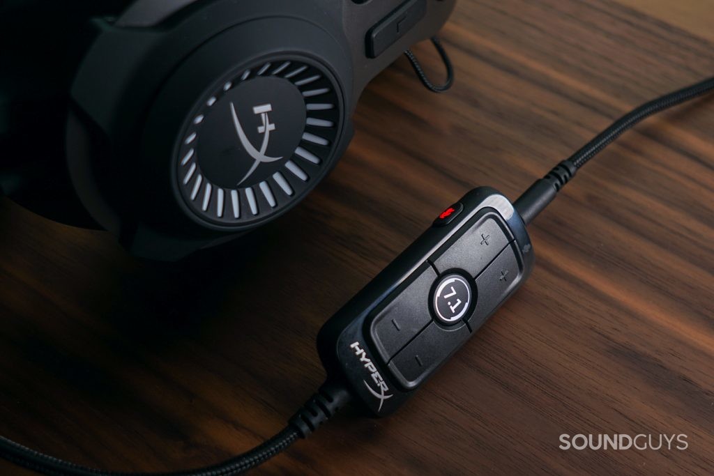 The HyperX Cloud Revolver + 7.1 gaming headset lays on a wooden table next to its 7.1 surround sound USB dongle with the mic muted and 7.1 turned on.