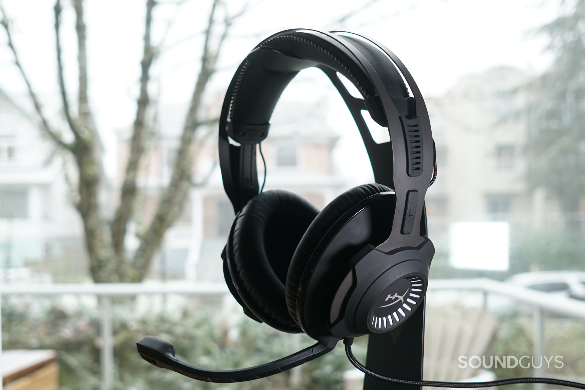 The HyperX Cloud Revolver + 7.1 sits on a stand by a window with snow falling lightly in the background.