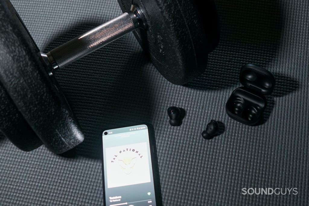 The Samsung Galaxy Buds Pro lay on an exercise mat by a dumbell, connected to a Google Pixel 4a running Spotify.