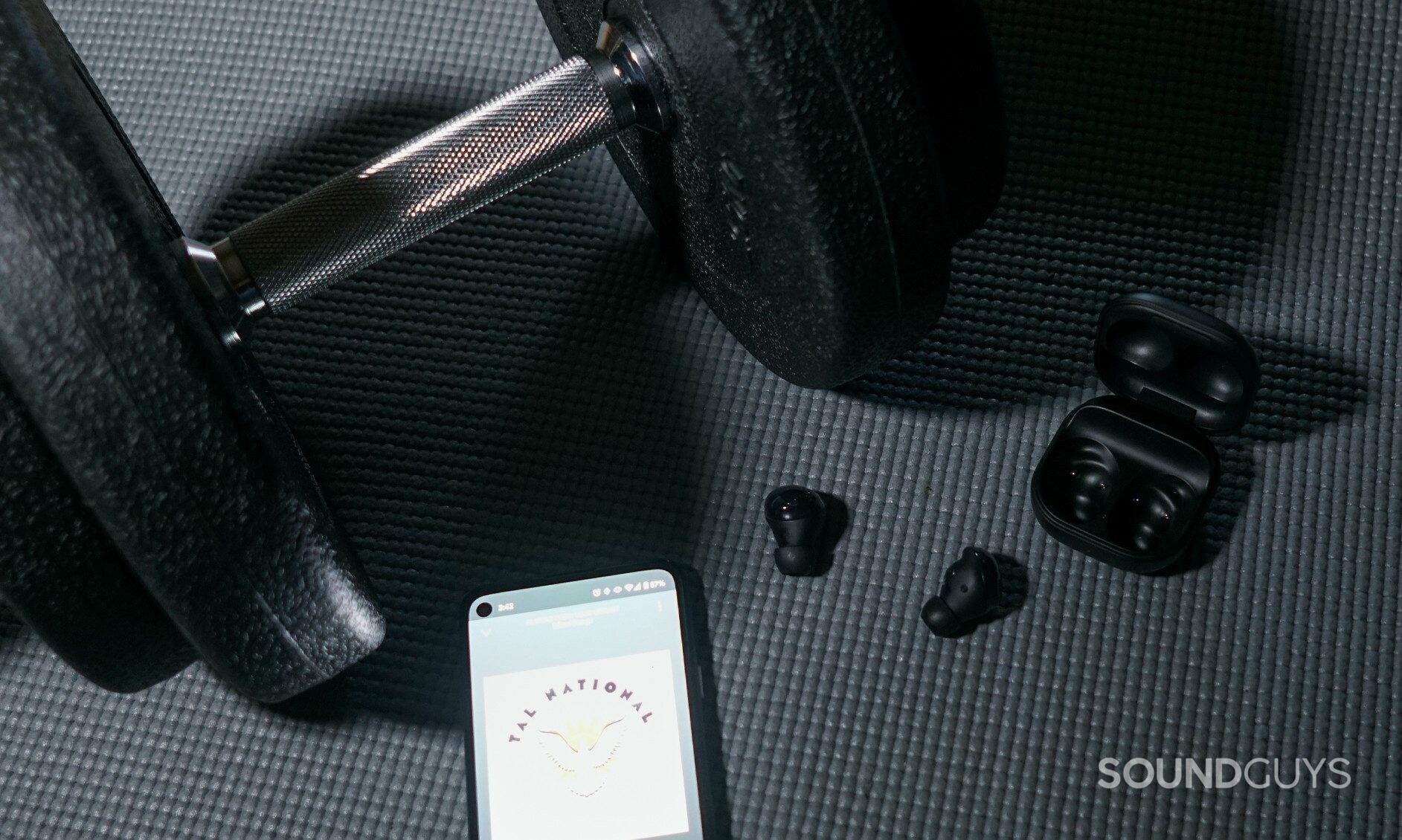 The Samsung Galaxy Buds Pro lay on an exercise mat by a dumbell, connected to a Google Pixel 4a running Spotify.