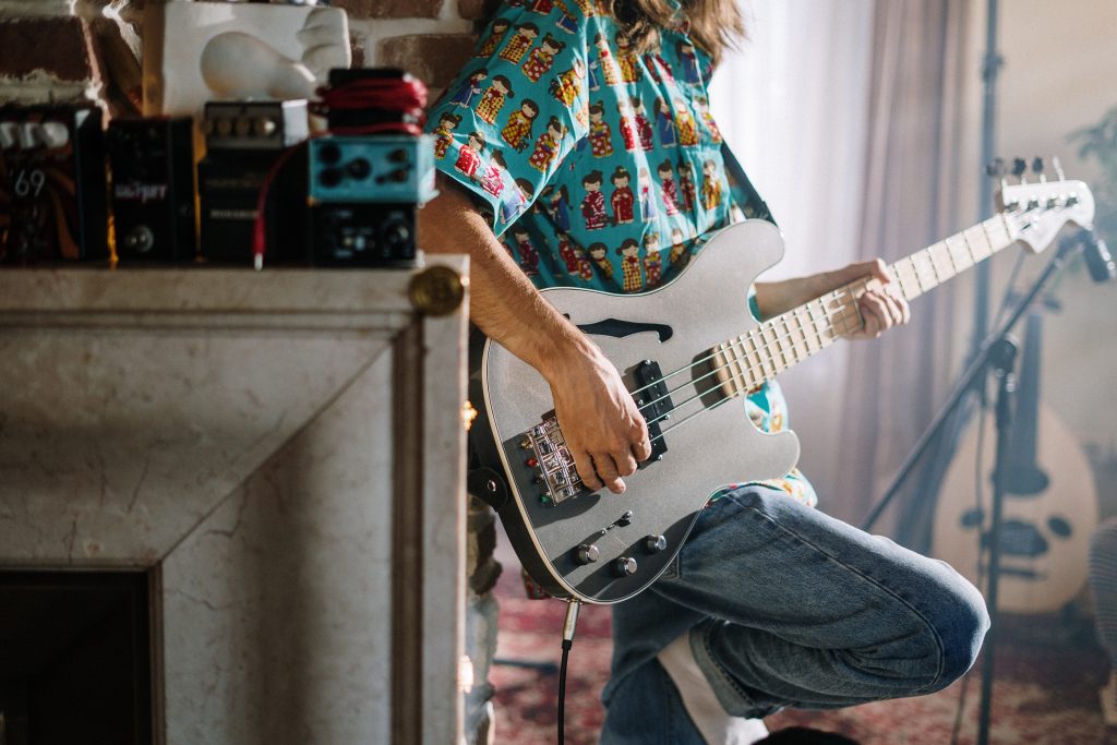 Man's torso and lower body leaning back against a shelf playing guitar.