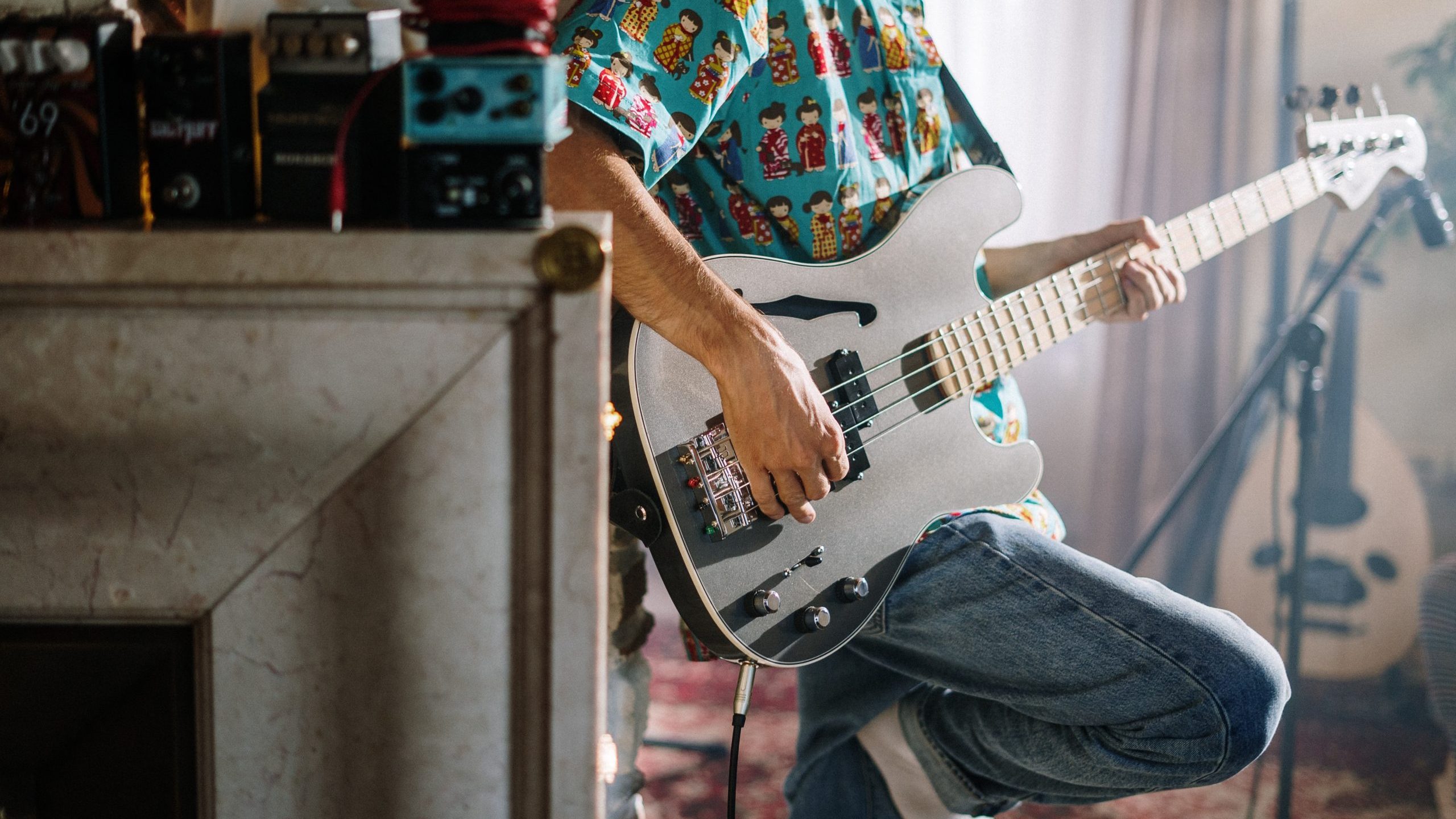 Man's torso and lower body leaning back against a shelf playing guitar.