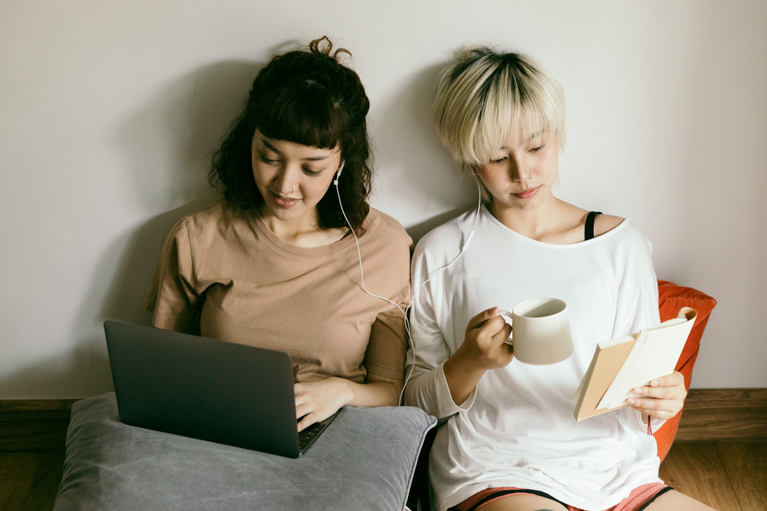 pexels-ketut-subiyanto-4126778 Two women sitting against a wall sharing a pair of wired earbuds.