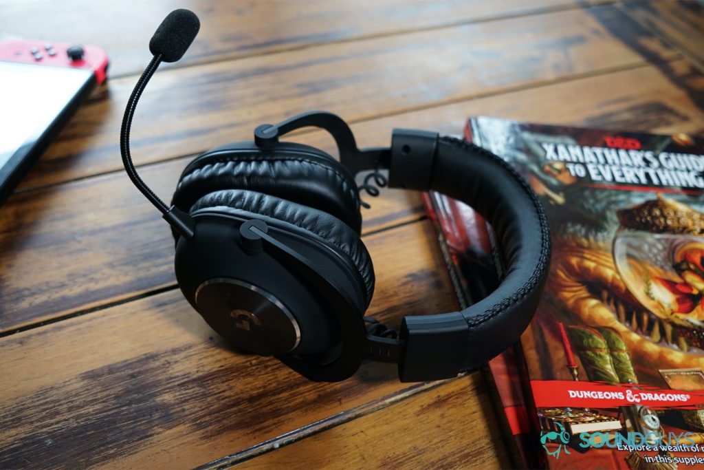 The Logitech G Pro X gaming headset lays on a wooden table leaning on a copy of Xanathar's Guide to Everything, with a Nintendo Switch in the background.