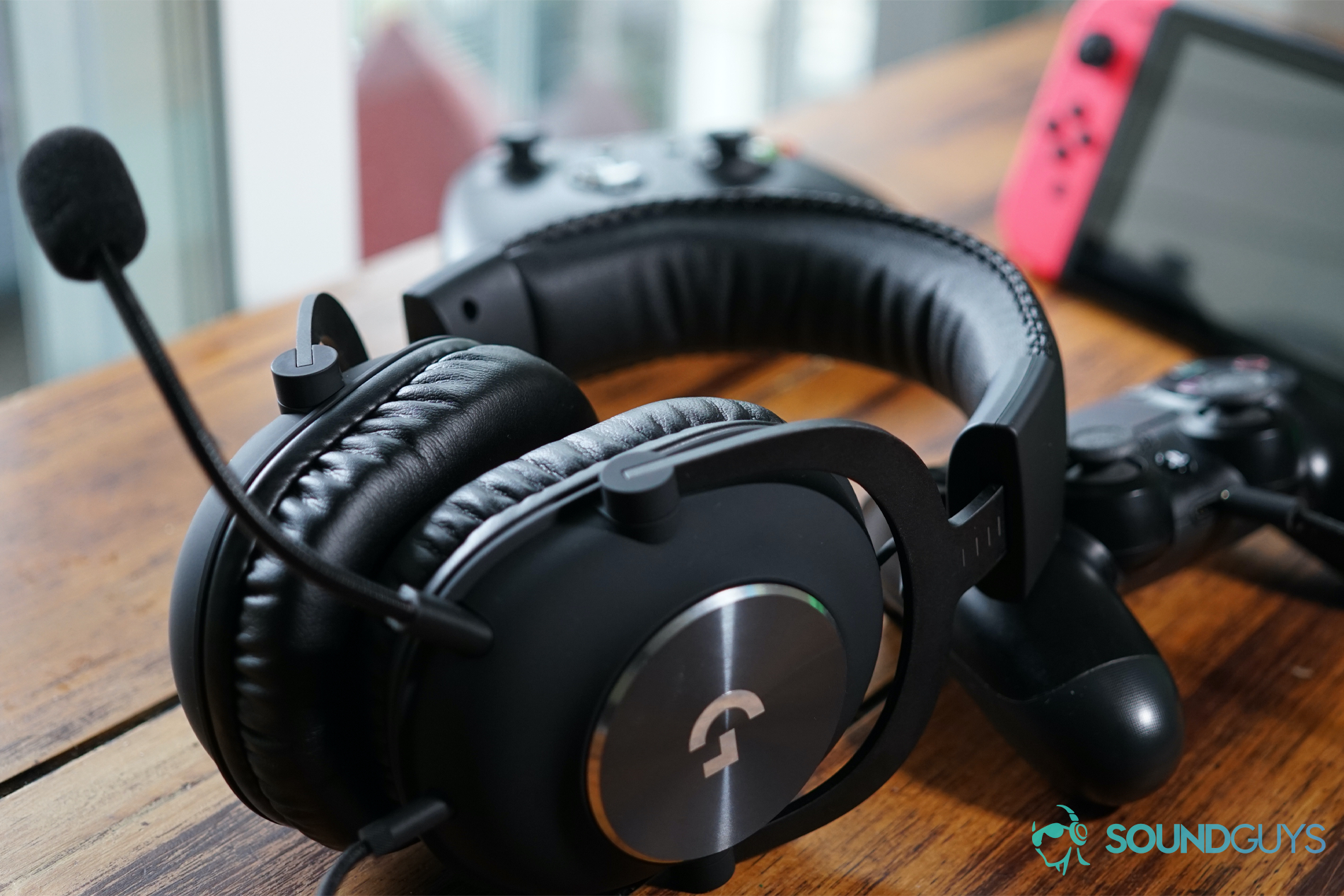 The Logitech G Pro X gaming headset leaning on a Playstation 4 controller, with a Nintendo Switch and an Xbox One controller in the background.