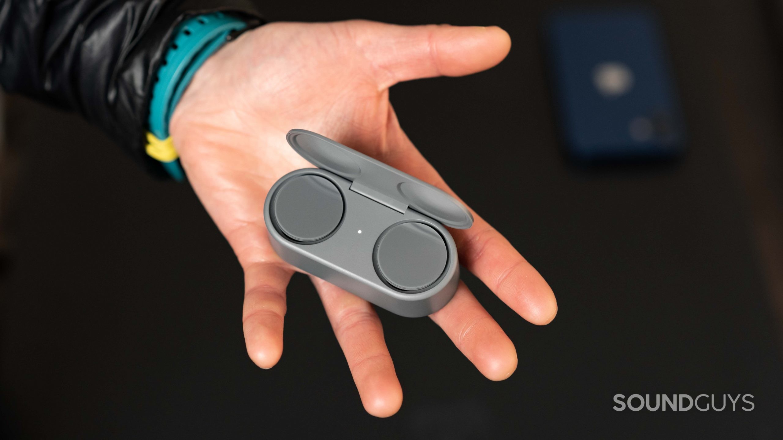 A hand holds the Microsoft Surface Earbuds open charging case.
